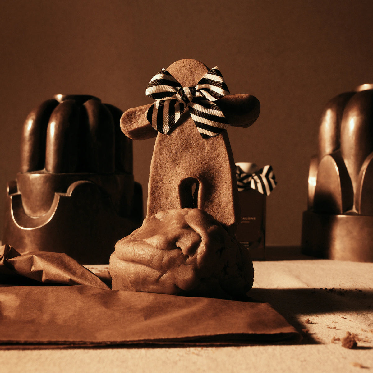 Jo Malone Ginger Biscuit Cologne behind a gingerbread figure with a striped bow.