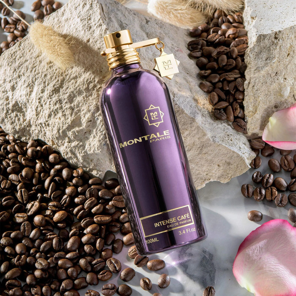 Flacon Montale Intense Café sur une pierre claire, entouré de grains de café et de pétales de rose.