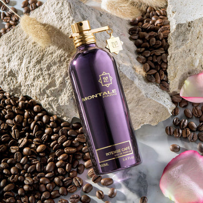Flacon Montale Intense Café sur une pierre claire, entouré de grains de café et de pétales de rose.