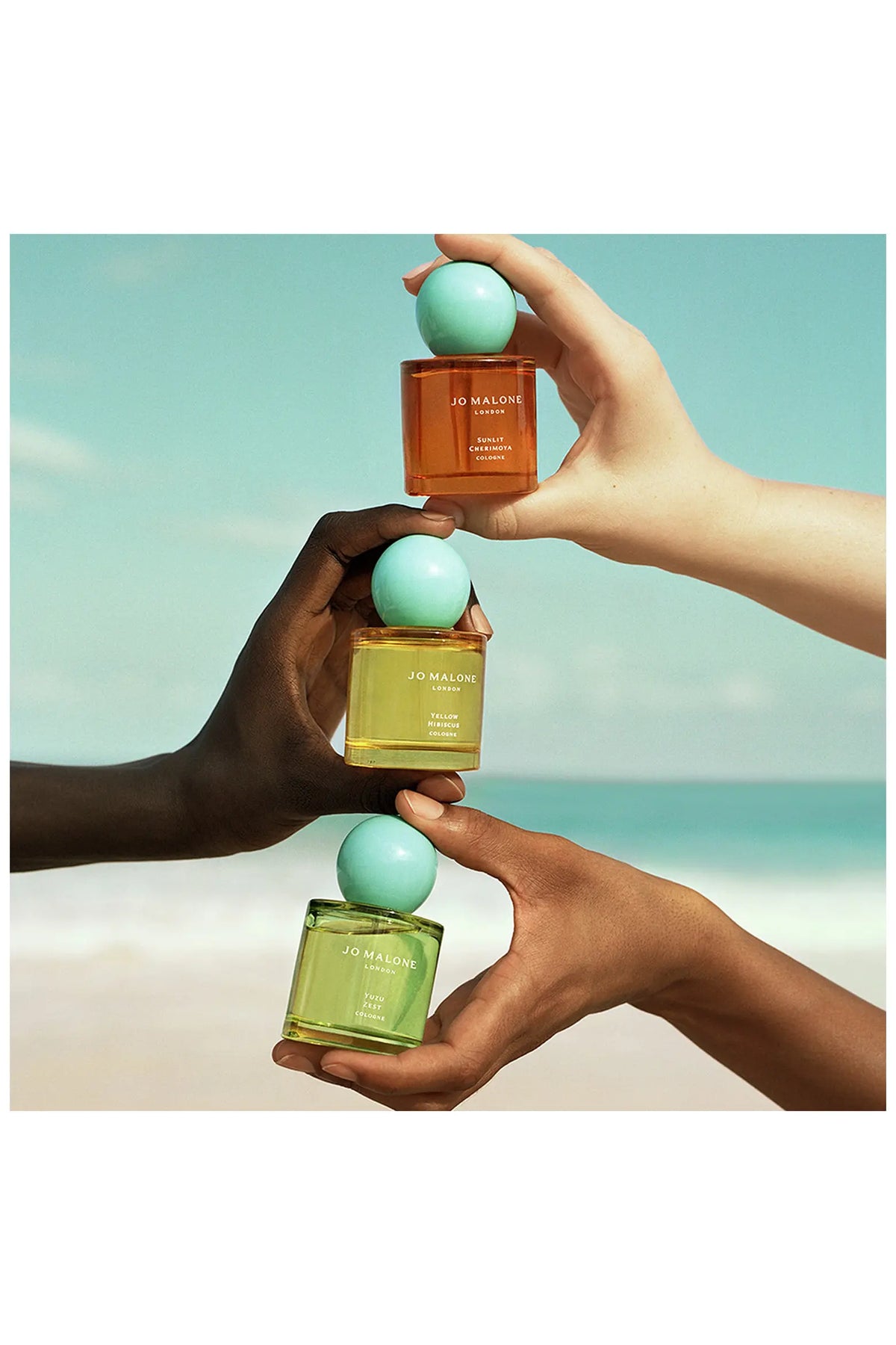Jo Malone Sunlit Cherimoya und zwei weitere Colognes mit türkisfarbenen Kugelkappen, von Händen gehalten.