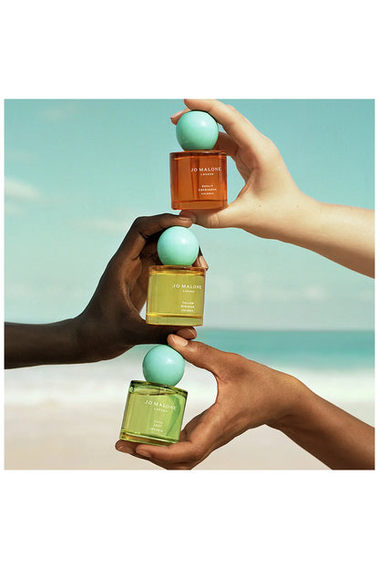 Jo Malone Sunlit Cherimoya und zwei weitere Colognes mit türkisfarbenen Kugelkappen, von Händen gehalten.